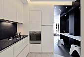 weiße minimalistische Designerküche, Frühstückstheke mit Hockern vor dunkler Wand im Durchgang