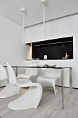 White classic shell chair around delicate table in front of kitchen units with black splashback