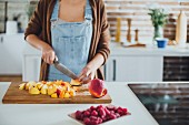 A woman cutting fruit on a wooden chopping board in a kitchen