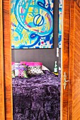 Bett mit lila Felldecke und buntes Bild spiegeln sich im Schrank