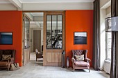 Zwei Sessel unter Bildern an orangener Wand vor einer Tür
