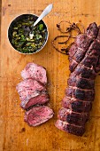 Smoked beef fillet on a chopping board next to a bowl of chimichurri sauce