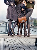 Three women wearing autumnal clothing standing on a bench