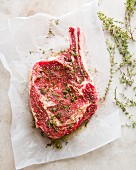 Rohes Ribeye Steak, gewürzt mit Salz, Pfeffer und Thymian, auf weißem Papier