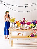 Laid table decorated with bouquets, in the background a woman dressed in summer with a wreath of flowers