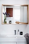 Weisser Waschtisch, darüber Wandspiegel mit Holzrahmen als Ablage mit Badutensilien