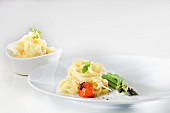 Tagliatelle with sautéed cherry tomatoes, basil and green asparagus with a bowl of mashed parsley potatoes in the background