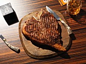 Grilled T-bone steak on a wooden plate with a steak knife