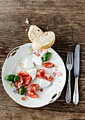 Mozzarella, tomato pieces, basil and baguette on a old floral-patterned porcelain plate