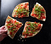 A hand taking a slice of bruschetta pizza