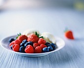 Raspberries, strawberries, blueberries and vanilla ice cream on white plate