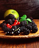 Blackberries, redcurrants, blackcurrants and an apple on a wooden plate