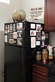 Schwarzer Kühlschrank mit Fotos dekoriert, oberhalb Globus und Schild in Küchenecke