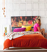 Young woman on double bed with orange velvet cover and colorful headboard
