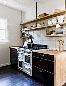 Black kitchenettes with wooden worktops and suspended wall shelves in front of wall tiles