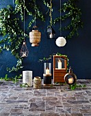 Hanging lamps in front of a wall painted dark blue, various lanterns with burning candles on tiled floors