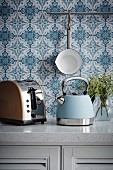 Retro teakettle and toaster on kitchen counter in front of blue and white wallpaper