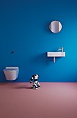 Minimalistisches Bad mit Toilette und Waschbecken an blauer Wand, Spielzeugroboter auf mauvefarbenem Boden
