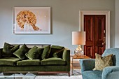 Green velvet sofa below picture on wall and table lamp on side table in elegant living area