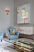 Glass coffee table with brass base, light blue armchairs and floating sideboard below mirrored wall-mounted cabinet