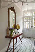 Retro console table below antique gilt-framed mirror in traditional hallway with Art-Nouveau stained glass panels in front door