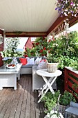 Veranda mit gemütlichem Ecksofa und Couchtisch, Küchenkräutern, Kletterrosen und Blumenampeln