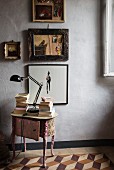 Antique, fabric-covered bedside table below pictures on wall