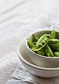 Fresh peas in pods in a white bowl