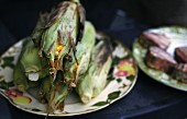 Grilled corn cobs with leaves and tuna fish steaks on a serving platter