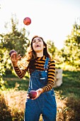 Junge Frau in Latzhose jongliert mit Äpfeln