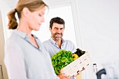 A middle-aged couple with a crate of vegetables in a kitchen