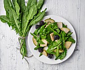 Dandelion salad with pears and blackberries on white wooden table