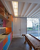 Colourful fitted kitchen with rustic workbench and view of bare trees through terrace doors