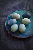 Blauer Teller mit natürlich gefärbten Ostereiern auf blauem Leinenstoff