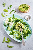 A green salad made of courgette spaghetti, Edamame beans, broccoli, water cress, bloodwort, baby spinach with ricotta, avocado bagel