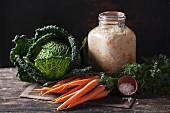 A jar of sauerkraut, savoy cabbage and a bundle of carrots on a rustic wooden table