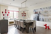 Upholstered dining chairs around table in front of large artwork on wall above Balloon Dog sculpture in red on floor