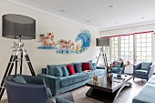 Zwei Stehleuchten mit transparentem Lampenschirm neben blauem Sofa und Kunstobjekt als Wanddekoration in elegantem Loungebereich