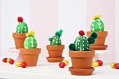 Blown eggs, painted and decorated as cacti in terracotta pots amongst scattered chocolate eggs