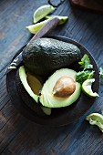 Avocados, whole and halved with a knife on a plate