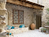 Gemauerte Sitzbank aus Naturstein mit Kissen unter verziertem Fensterladen in mediterranem Innenhof