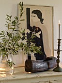 Olivenzweig in Glasgefäss, Holzschale, Kerzenhalter und Bild mit Frauenmotiv auf weisser Ablage