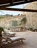 Holzliegen und Tisch mit Stühlen auf mediterraner Terrasse mit Terrakottafliesenboden und Natursteinwänden