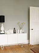 Weisses Sideboard mit Vasen, Büchern und Tischleuchte vor grauer Wand in Altbauwohnung mit Dielenboden
