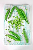 Peas and pea pods on a chopping board (seen from above)