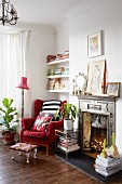 Red velvet wing-back chair next to artistic fire surround in cosy reading corner