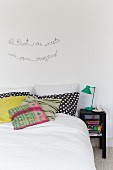 Bett mit verschiedenen Kissen und Sinnspruch an Wand