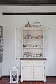 Silver and gold crockery in vintage dresser next to white lantern