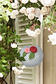 Romantic, knitted lantern decorated with knitted flowers below white climbing rose in front of external shutters