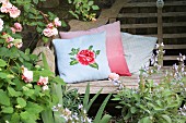 Romantischer, gestrickter Kissenbezug mit Rosenmotiv auf rustikaler Gartenbank